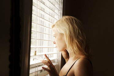 Seitenansicht einer Frau, die durch einen Fensterladen zu Hause schaut - CAVF10354