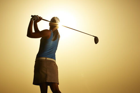 Die Sonne scheint hinter einer Frau, die einen Golfschläger schwingt - CAIF19548