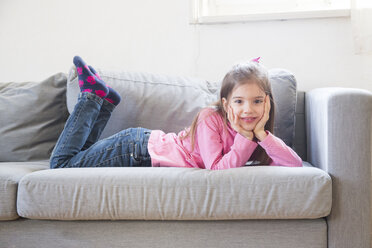 Portrait of smiling little girl lying on the couch - LVF06792