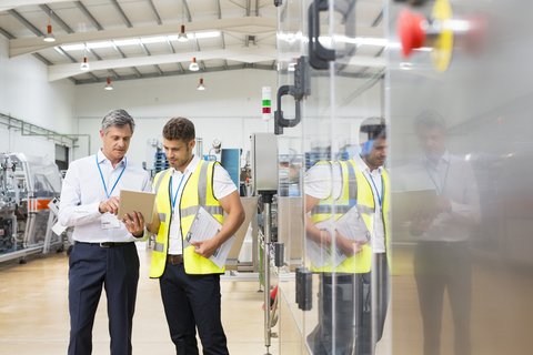 Vorgesetzter und Arbeiter verwenden digitales Tablet in einer Fabrik, lizenzfreies Stockfoto