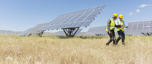 Workers walking by solar panels in rural landscape - CAIF19650