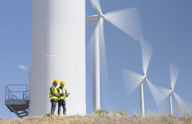 Workers talking by wind turbines in rural landscape - CAIF19656