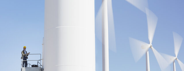 Worker standing on wind turbine in rural landscape - CAIF19660