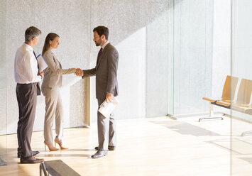 Business people shaking hands in sunny office lobby - CAIF19692