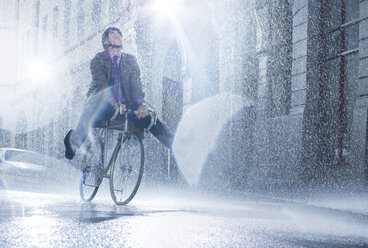 Geschäftsmann fährt Fahrrad in regnerischer Straße - CAIF19706