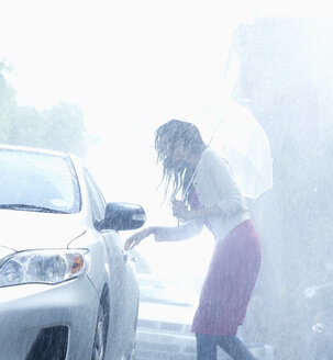 Frau mit Regenschirm greift im Regen nach dem Türgriff eines Autos - CAIF19711