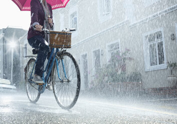 Woman riding bicycle with umbrella in rainy street - CAIF19712