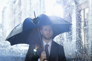 Frustrierter Geschäftsmann mit kaputtem Regenschirm im Regen - CAIF19713