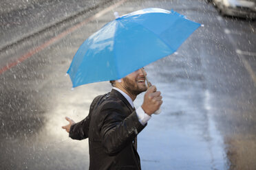 Businessman with tiny umbrella walking in rain - CAIF19716