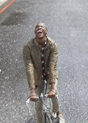 Enthusiastic man riding bicycle in rain - CAIF19723