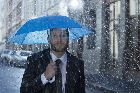 Porträt eines Geschäftsmannes mit kleinem Regenschirm im Regen, lizenzfreies Stockfoto