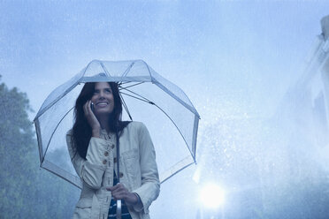 Geschäftsfrau telefoniert unter Regenschirm im Regen - CAIF19729