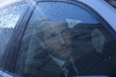 Nahaufnahme eines Geschäftsmannes im Auto, der in den Regen blickt - CAIF19730