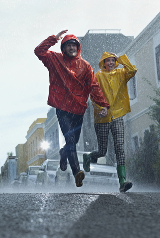 Happy couple in raincoats running down street in rain stock photo