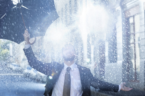 Enthusiastischer Mann mit kaputtem Regenschirm im Regen, lizenzfreies Stockfoto