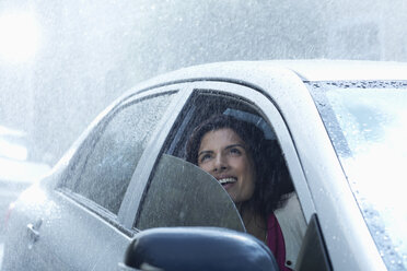 Lächelnde Geschäftsfrau im Auto, die in den Regen blickt - CAIF19737