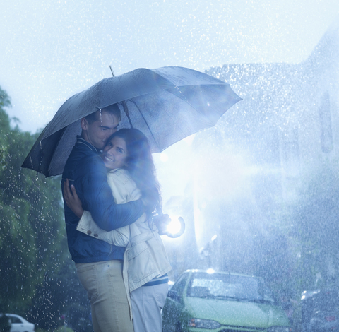 Glückliches Paar, das sich im Regen unter einem Regenschirm umarmt, lizenzfreies Stockfoto