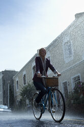 Happy woman riding bicycle in rainy street - CAIF19742