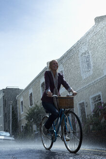 Glückliche Frau fährt Fahrrad in einer verregneten Straße - CAIF19742