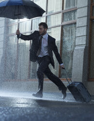 Geschäftsmann mit Koffer und Regenschirm beim Überqueren einer regnerischen Straße - CAIF19748