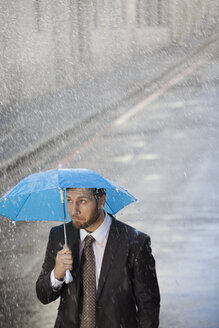 Geschäftsmann unter kleinem Regenschirm in regnerischer Straße - CAIF19761