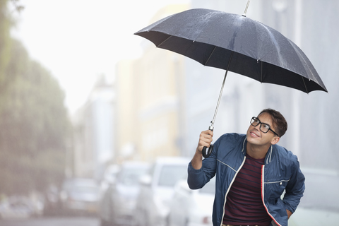 Mann mit Regenschirm schaut auf Regen auf der Straße, lizenzfreies Stockfoto