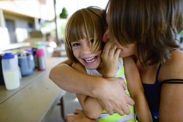 Mutter küsst und umarmt glückliche Tochter, während sie am Tisch im Hof sitzt - CAVF10378