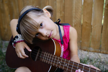Porträt eines Mädchens, das an einem Holzzaun sitzend Gitarre spielt - CAVF10389