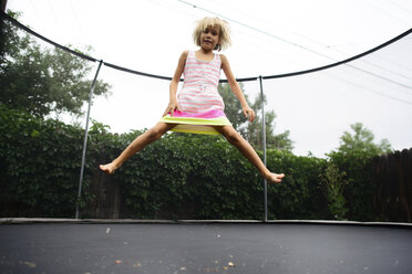 Low angle portrait of girl jumping on trampoline at park against clear sky - CAVF10392