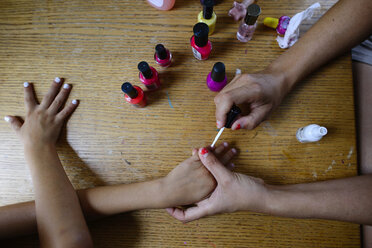 Draufsicht auf die Mutter, die zu Hause Nagellack auf die Fingernägel ihrer Tochter aufträgt - CAVF10395