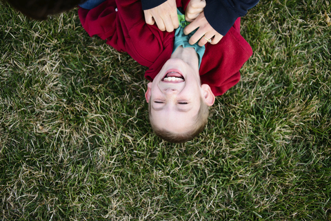 Draufsicht auf die Mutter, die ihren Sohn auf einer Wiese liegend kitzelt, lizenzfreies Stockfoto