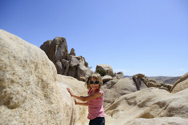 Porträt eines Mädchens, das an den Felsen im Joshua Tree National Park steht, gegen einen klaren Himmel an einem sonnigen Tag - CAVF10399