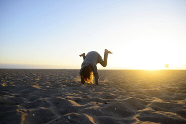 Girl practicing handstand at beach against clear sky during sunrise - CAVF10404