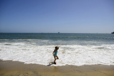 Verspieltes Mädchen läuft auf den Wellen am Seal Beach gegen den klaren Himmel - CAVF10406