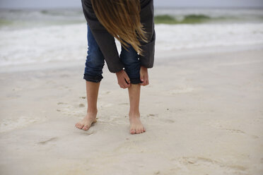 Girl rolling up jeans at beach - CAVF10412