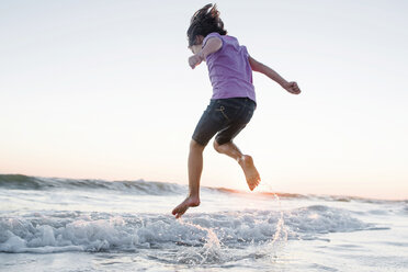 Low angle view of girl jumping on waves at beach against clear sky during sunset - CAVF10414