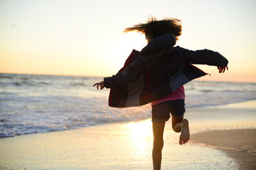 Rear view of playful girl running on shore against clear sky during sunset - CAVF10416