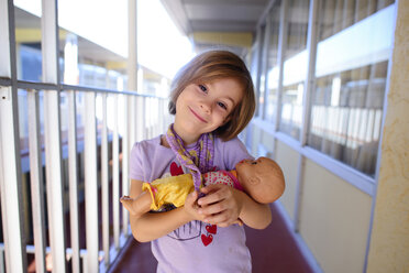 Portrait of happy girl carrying doll in corridor - CAVF10420