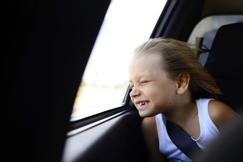 Mädchen genießt den Wind, während sie im Auto am Fenster sitzt, lizenzfreies Stockfoto