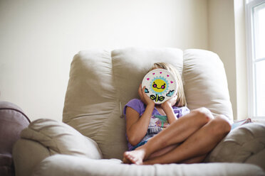 Mädchen hält Spielzeug gegen ihr Gesicht, während sie auf der Couch gegen die Wand sitzt - CAVF10432