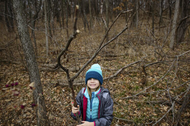 Hochformatiges Porträt eines Mädchens, das einen getrockneten Zweig hält, während es im Wald steht - CAVF10445