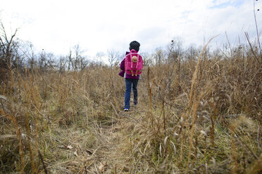 Rear view of girl with backpack walking on dry grassy field - CAVF10446