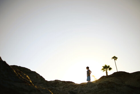 Niedriger Blickwinkel auf einen Jungen, der auf einer Felsformation vor dem klaren Himmel am Laguna Beach steht - CAVF10450
