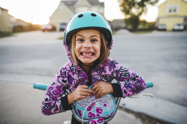 Porträt eines verspielten Mädchens, das die Zähne zusammenbeißt, während es auf dem Fußweg einen Motorroller fährt - CAVF10459