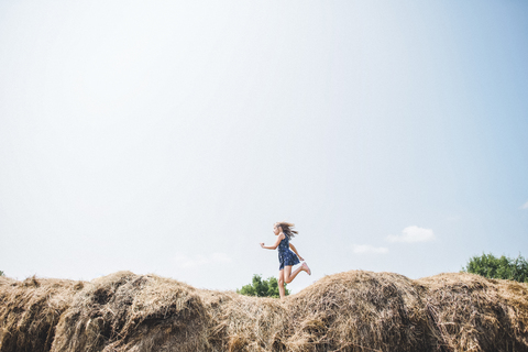 Unbekümmertes Mädchen läuft auf einem Heuhaufen gegen den Himmel, lizenzfreies Stockfoto