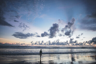 Rückansicht einer am Strand stehenden Frau gegen einen bewölkten Himmel bei Sonnenuntergang - CAVF10474
