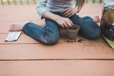 Tiefschnitt eines Mädchens, das auf der Veranda sitzend Samen in einen Topf pflanzt - CAVF10484