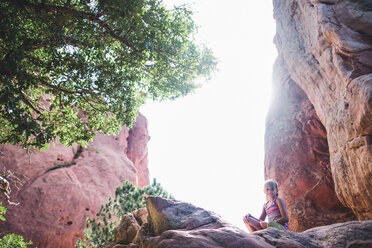 Low angle portrait of girl sitting on rocks against clear sky - CAVF10487