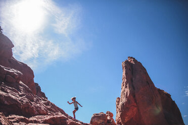 Low angle view of carefree girl climbing on rock formation against sky - CAVF10489