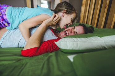 Seitenansicht der verspielten Tochter leckt die Wange der Mutter auf dem Bett zu Hause - CAVF10499